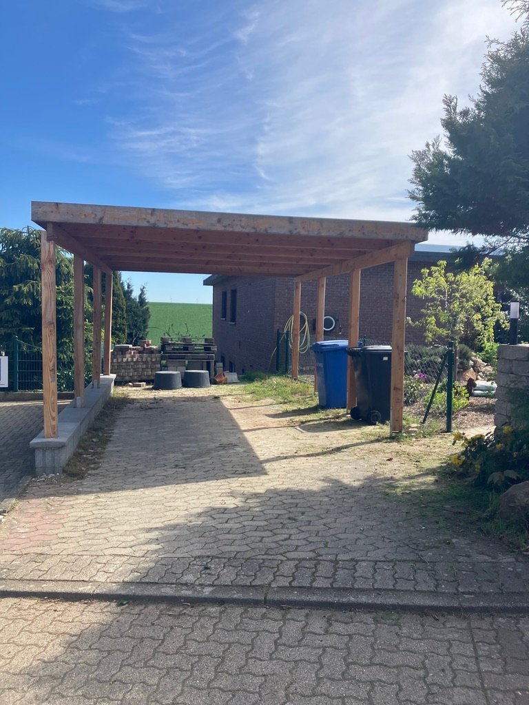 Carport mit unfertigem Schotter-Boden, Mülltonnen und gestapeltem Pflastermaterial
